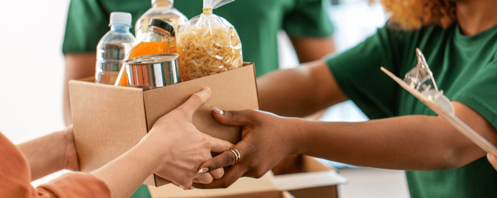 Woman handing another person a box of food and goods to donate