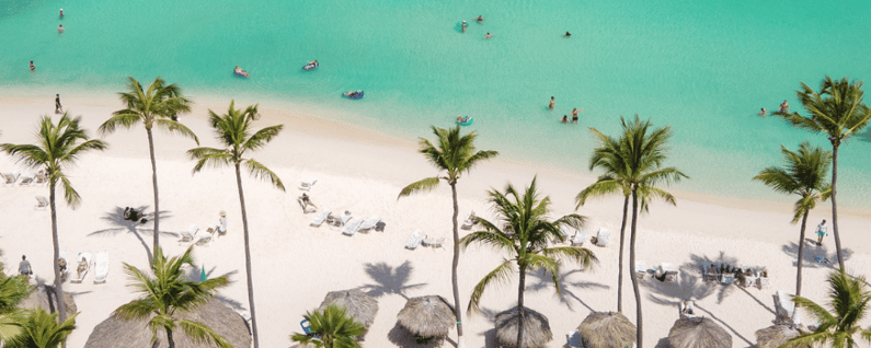 beachside with palm trees and huts and people playing in water on beach