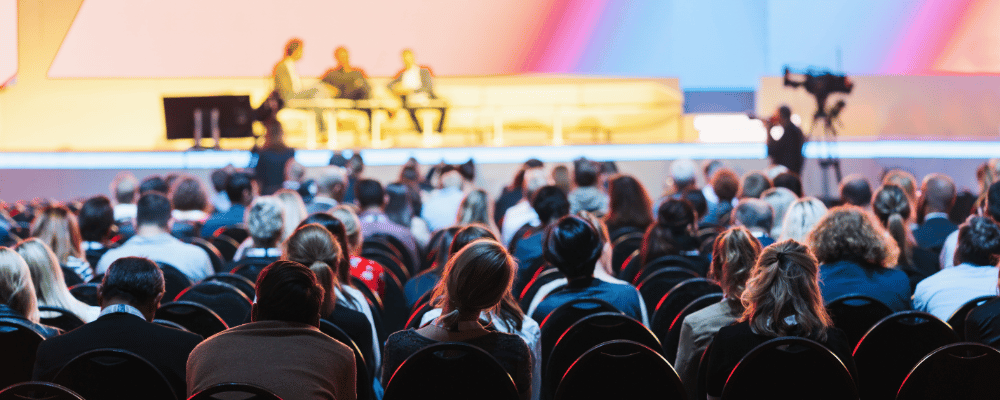 People sitting in front of a stage watching a conversation onstage in a large convention city