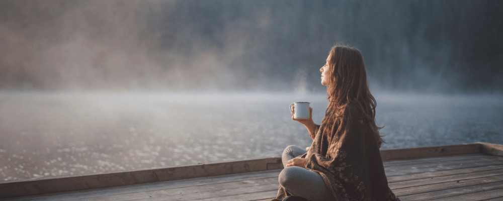 woman enjoying solitude on a dock with a cup of coffee at her executive wellness retreat