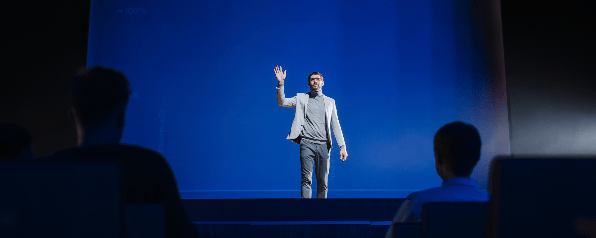 Man standing on stage hosting a keynote while waving to the audience