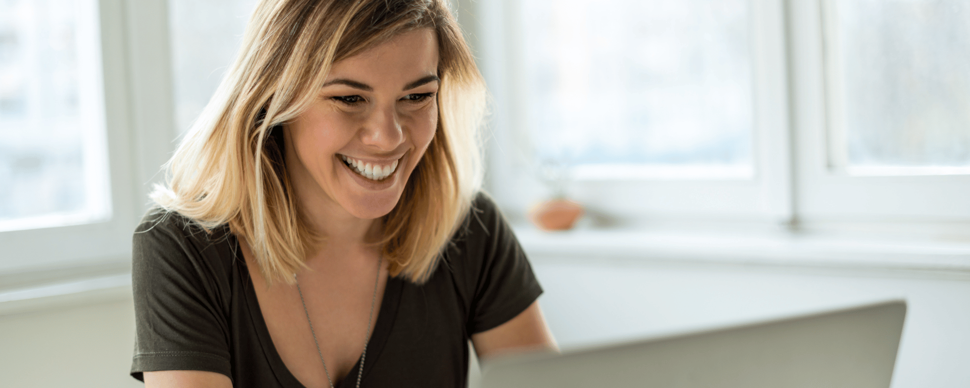 woman smiles as she sits at her computer planning an upcoming sales kickoff meeting