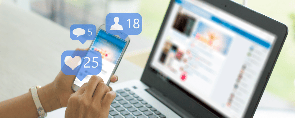 person checking social media on phone and laptop with like and comment bubbles floating above